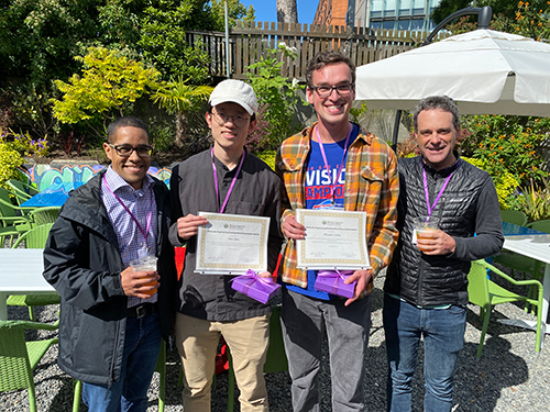 Two faculty standing with two students holding certificates.