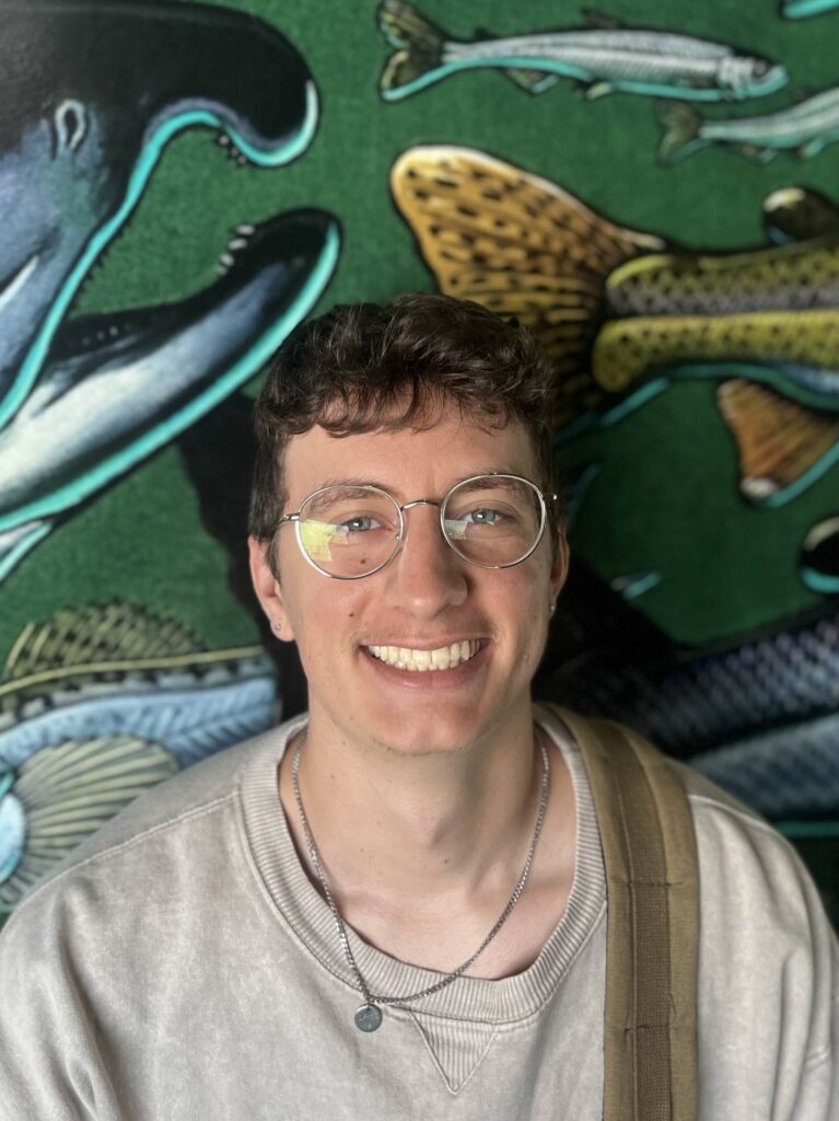 Zach in front of a colorful background with images of fish and other sea life.
